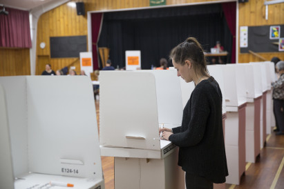 A woman in a school hall on election day, filling in her voting paper in a voting booth.
